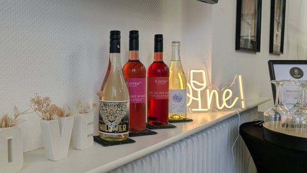 Roséweine und ein Weißwein auf der Fensterbank neben einem leuchtenden Wine-Schriftzug
