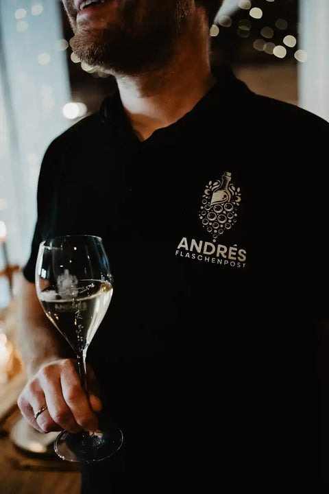 Gastgeber im Poloshirt von Andrés Flaschenpost mit einem Glas Weißwein beim Sektempfang