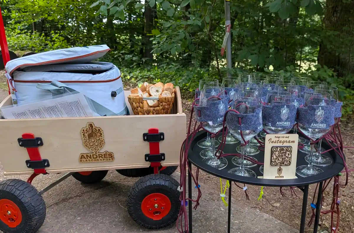 Bollerwagen mit Kühltasche und Brotkorb, daneben Weingläser in Filzhaltern für eine Weinwanderung