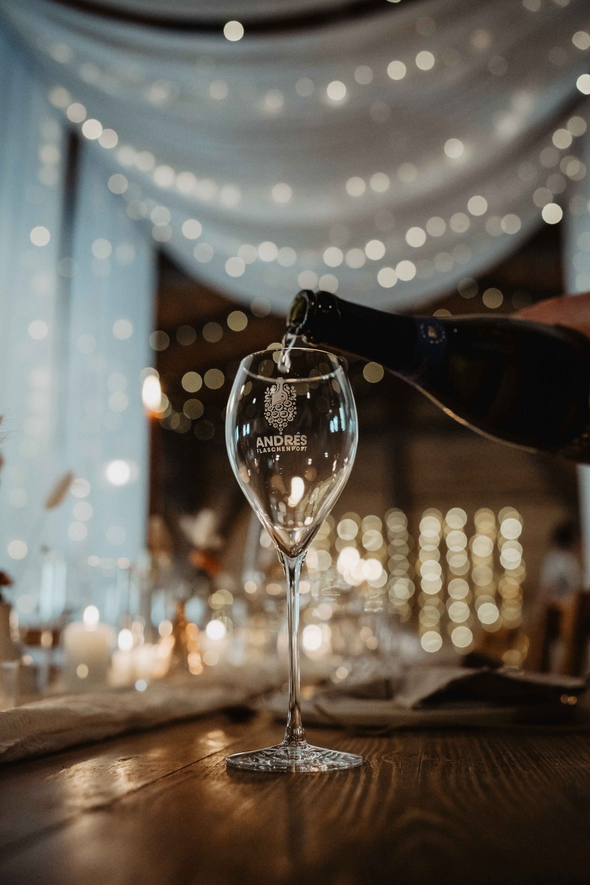 Winzersekt wird in ein Glas von Andrés Flaschenpost eingeschenkt, im Hintergrund Lichterketten
