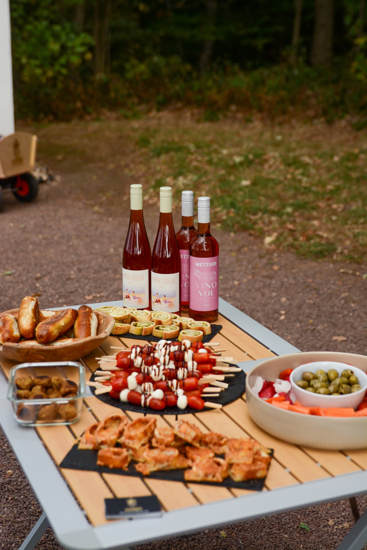 Snackplatte mit Tomate-Mozzarella-Spießen, Gebäck und Oliven neben Roséweinen
