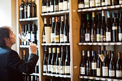 Ein Mann steht vor einem Regal und schaut viele verschiedene Flaschen Wein an