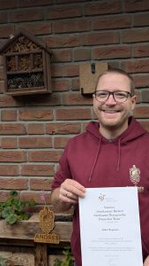 Mann hält Weinzertifikat vor Backsteinwand